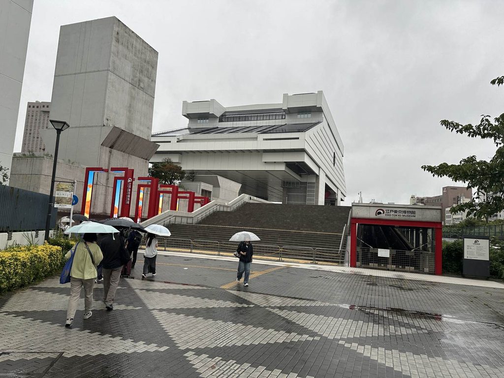 雨の中、傘を差して江戸東京博物館へ向かう人たち。高床式の独特な建物が見える