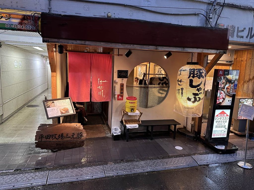 両国「とんかつ はせ川」の店構え。赤いのれんと大きな提灯、店先にベンチがある